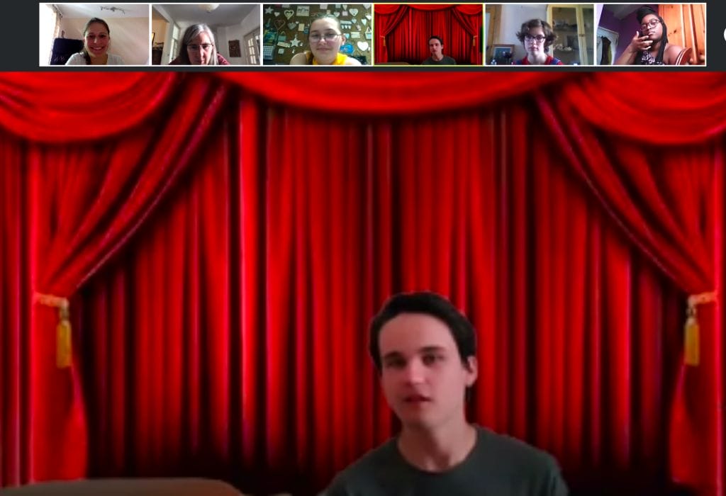 Cameron looks to camera against a Zoom background of red stage curtains with small images of other participants above